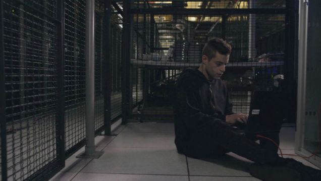 A hacker works on a laptop inside a security cage