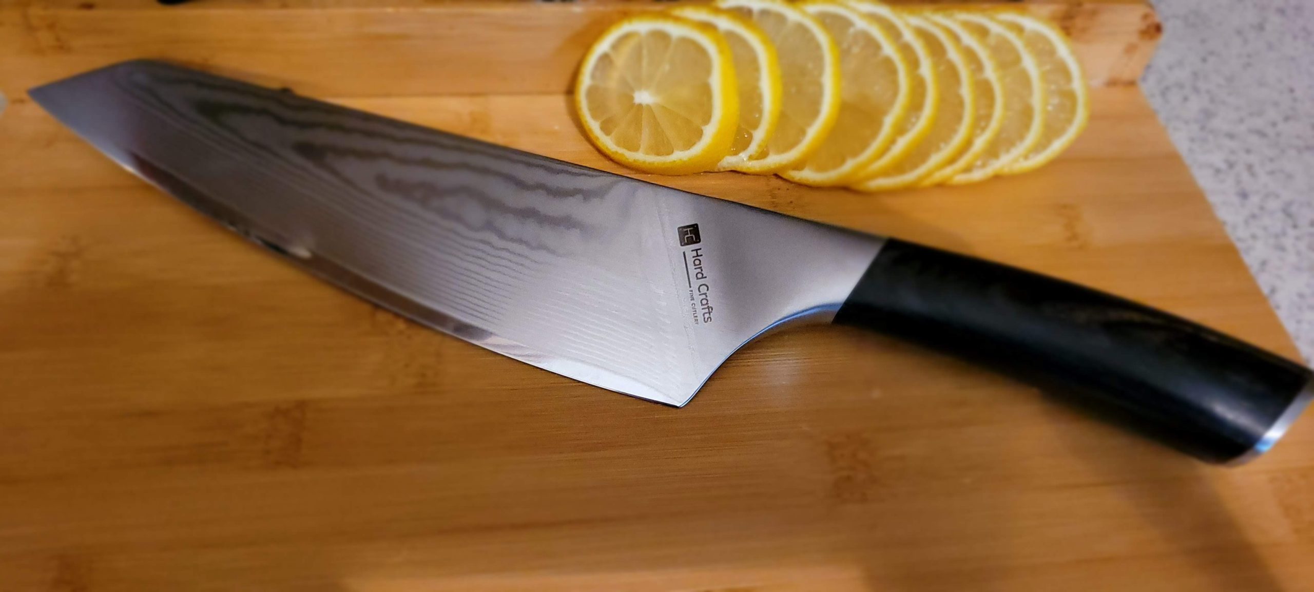 A Damascus steel knife on a cutting board with sliced lemon.